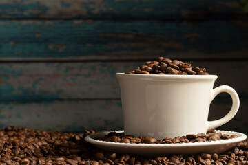 Front view of Coffee cup filled with coffee beans on a table with scattered coffee beans
