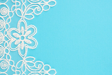 White lace with flowers and leaves on blue vertically with copy space