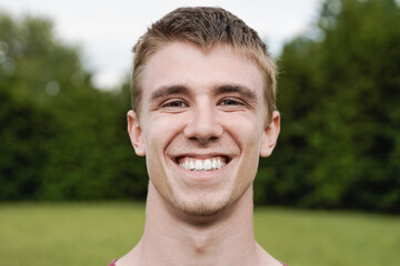 Young happy man smiling and looking at camera outdoor at city park - Focus on face