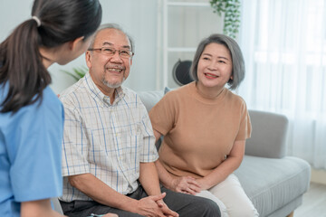 Asian elderly smiling sitting on sofa while young woman caregiver doctor give consultation about health in living room during home visit