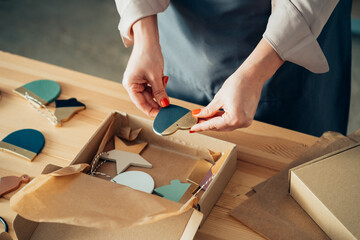 High angle view of unrecognizable woman potter packing merchandise for delivery in a cardboard box while standing at her workshop desk