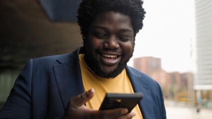 Happy curvy African man using mobile smartphone outdoor