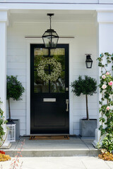 front door to a modern farmhouse with a pair of topiaries