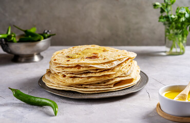 Homemade Indian flat bread Chapati or Roti on grey concrete background with butter ghee, hot green pepper and coriander