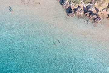 People swim or relax, turquoise sea water and sandy beach with rocks, aerial view. Summer vacation.