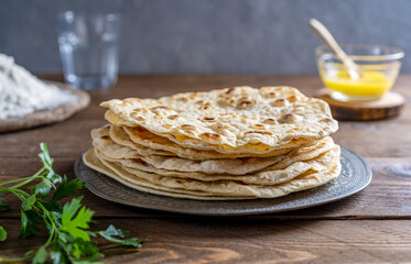 Homemade Indian flat bread Chapati or Roti on wooden background with butter ghee, flour, water and cilantro