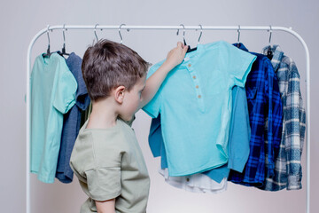 Boy preschooler standing by the hangers, racks up clothes, and chooses clothes for today