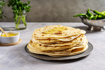 Homemade Indian flat bread Chapati or Roti on grey concrete background with butter ghee, hot green pepper and coriander