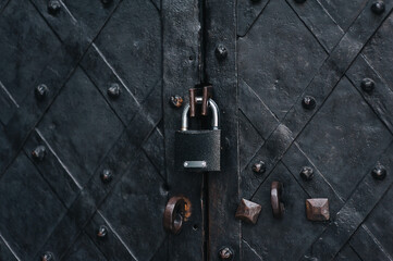 Padlock on an old forged black metal door with stripes and rivets. Fragment of the Boim Chapel in Lviv, Ukraine. Vintage background closeup. Closed passage and protection concept.