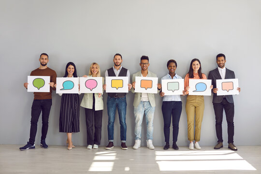 Everyone has their own opinion. Portrait of group of men and women holding white sheets of paper with empty colored speech bubbles on them. Multiracial people standing near wall and empty room.