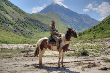A man is sitting on a horse. In the background are high mountains.