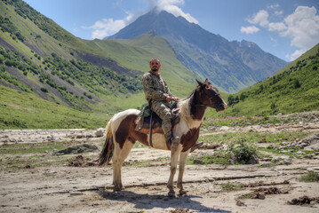 Naklejka premium A man is sitting on a horse. In the background are high mountains.