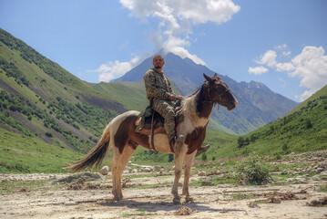 A man is sitting on a horse. In the background is a mountain valley.