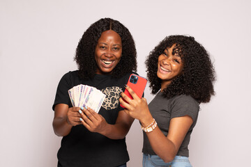 two african girls feeling excited holding money and phone