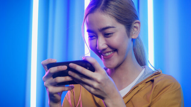 Gamer woman controlling smart phone for video game. Teenage girls leisure game in neon light room at home.