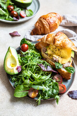 Croissant with tuna, poached egg, avocado and hollandaise sauce with salad leaves and tomatoes. Croissant sandwich with egg benedict and tuna.