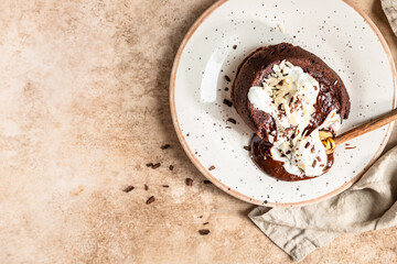 Chocolate fondant or lava cake with whipped cream, almond and chocolate pieces, brown background....