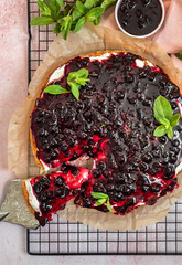 Tart with creamy filling made of cream cheese or mascarpone with black currant sauce and mint on metal grille, pink background. Dessert with cream and berry sauce. Top view.