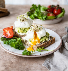 Sourdough bread with cream cheese, mashed avocado and poached egg with salad leaves, tomatoes and sprouts on concrete background. Healthy breakfast or brunch. Diet food concept.