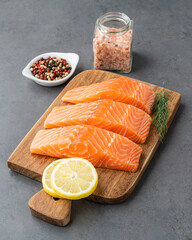 Raw salmon slices with seasonings over wooden board