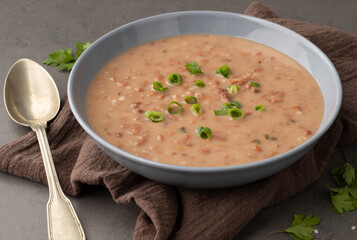 Brown bean soup in a bowl with seasoning over stone background