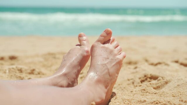Female foot with hallux valgus close up on the beach on vacation summer day. Woman with foot deformation halluxvalgus enjoy summer sandy beach. 