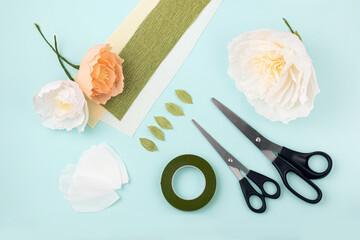 Hand made crepe paper flowers, leaves, scissors and floral tape flat lay.  Paper peony DIY concept