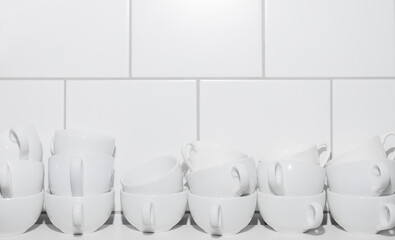 Fototapeta na wymiar In two rows of white cups on a white table on a background of white tiles. Copy space