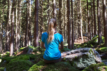 Woman sitting in green forest enjoys the silence and beauty of nature.