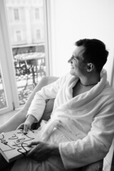 in the photo, a smug man in a bathrobe in hotels lying down enjoying the view from the window