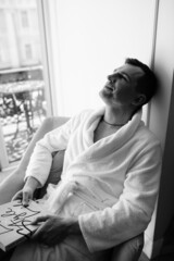 in the photo, a smug man in a bathrobe in hotels lying down enjoying the view from the window