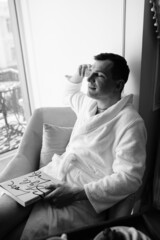 in the photo, a smug man in a bathrobe in hotels lying down enjoying the view from the window