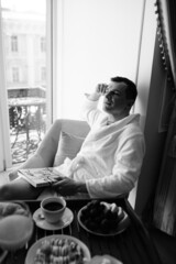 in the photo, a smug man in a bathrobe in hotels lying down enjoying the view from the window