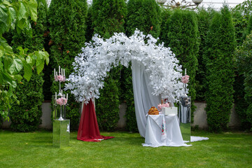 Wedding arch of white flowers and other elements of wedding design on the green lawn