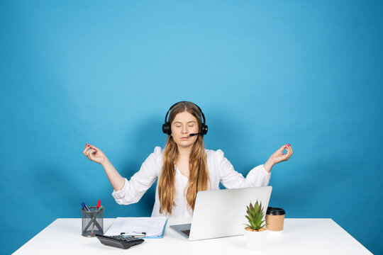 Virtual assistance worker meditating and relaxing sitting behind desk. Young pretty telemarketing worker isolated on blue background.