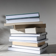A stack of books are on a beige table against a white wall. Scandinavian style. Minimalism. Place...