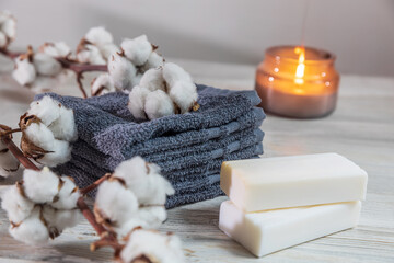 Four gray terry face towels, two bars of soap, a candle in a glass jar, and a branch of cotton at the spa. Beauty saloon. Comfort and care