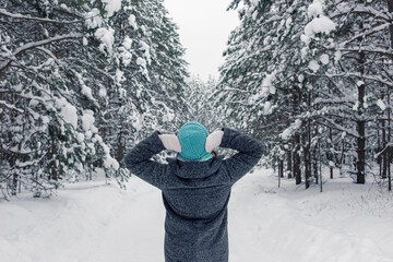 a girl stands in a beautiful winter snowy forest, raising her hands to her head, examines the trees.