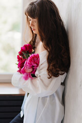 a beautiful young brunette woman in a white shirt with a bouquet of peonies.