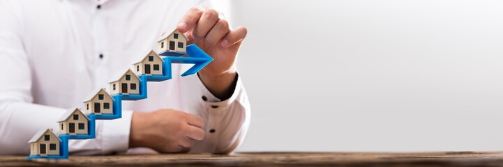 Businessman placing house models on increasing arrow staircase