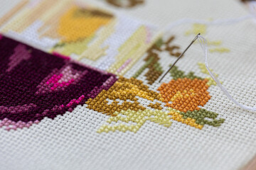 Cross-stitch embroidering in progress. Young girl in linen clothes is doing handmade embroidery