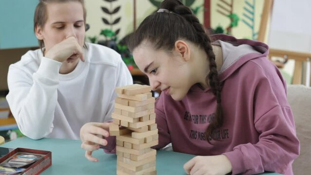 two girls with disabilities are playing a board game sitting at a large table. Rehabilitation of people with disabilities.