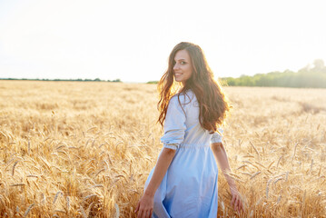 A young woman walks through a wheat field and looks at the camera.