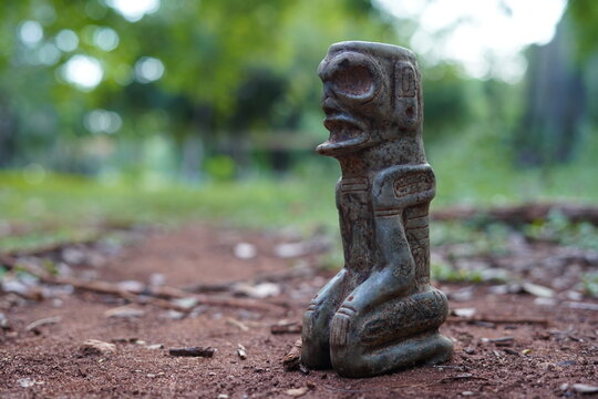 Taino Antique Kneeling meditative Stone Cemi Idol God Figure standing over red dirt on the ground, close up. Taino Mythology.