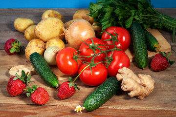 Potatoes, ginger, strawberries, fruits, onions, parsley, dill, tomatoes, cucumbers lie on a wooden table
