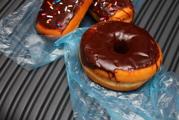 Chocolate donuts and chocolate donut bars topped with multicolored sugar flakes. Placed on a gray...