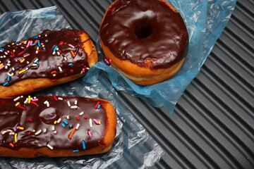 Chocolate donuts and chocolate donut bars topped with multicolored sugar flakes. Placed on a gray...