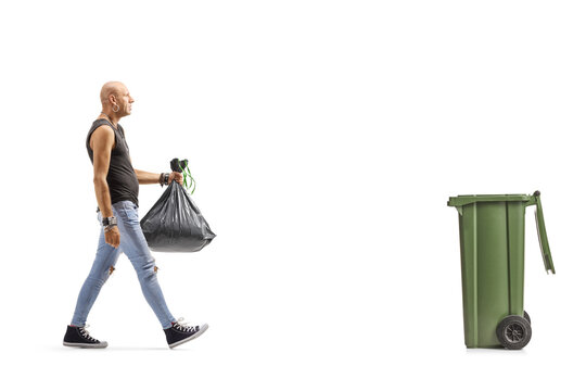 Bald Man In Ripped Jeans Carrying A Plastic Waste Bag And Walking Towards A Dustbin