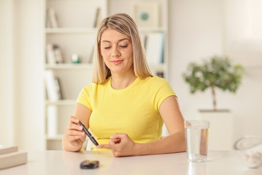 Young woman sitting at home and checking blood sugar level with a pen