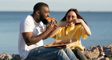 Diverse couple eating pizza and having fun. Seaside vacation.